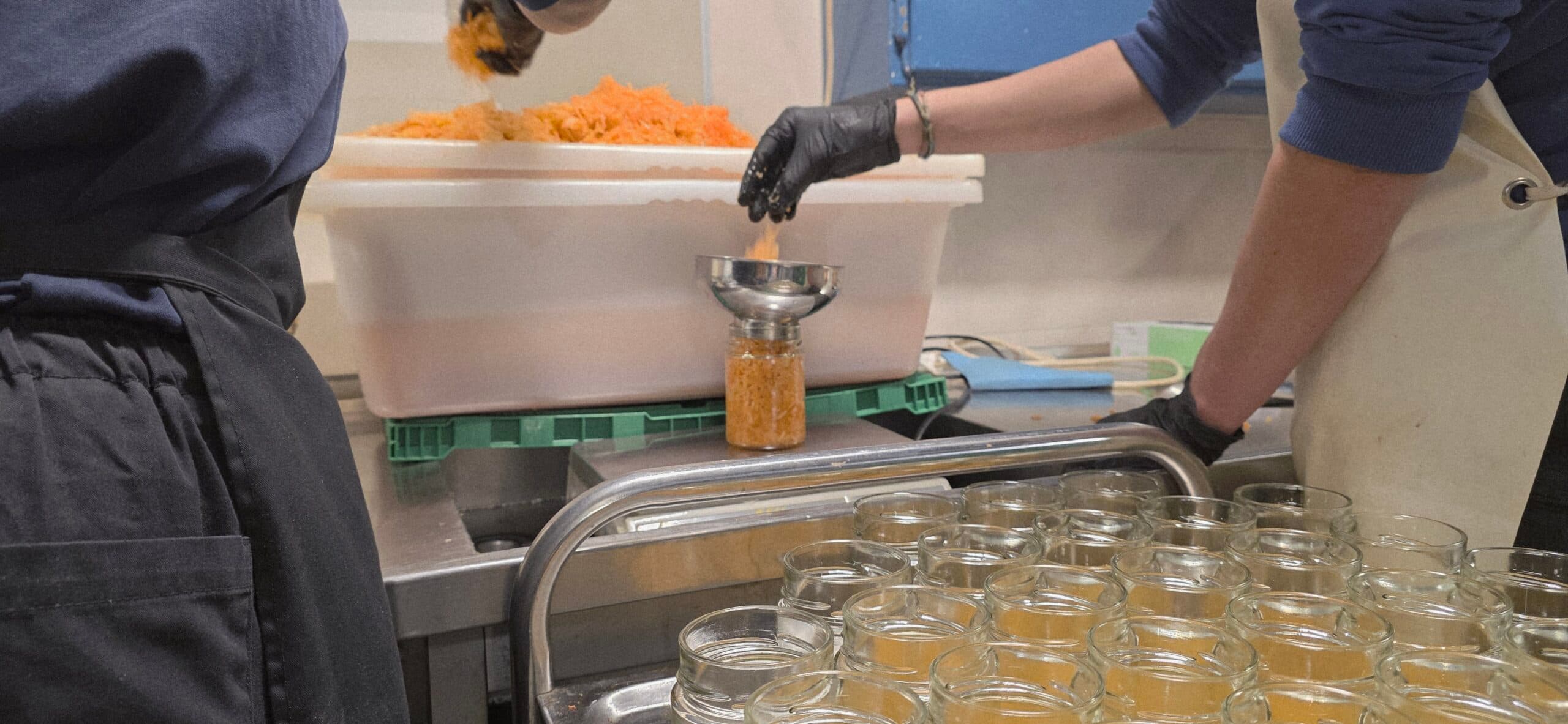 Mise en bocaux d'une préparation lactofermentée à l'atelier : entonnoir, bac de préparation et bocaux vides